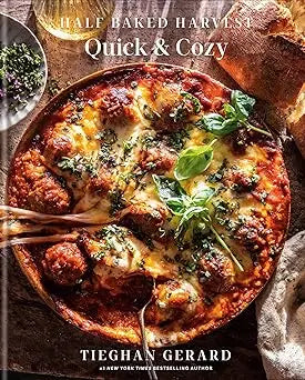 A rustic wooden spoon rests in a golden-brown cheesy meatball pizza with fresh basil from half baked harvest quick cozy